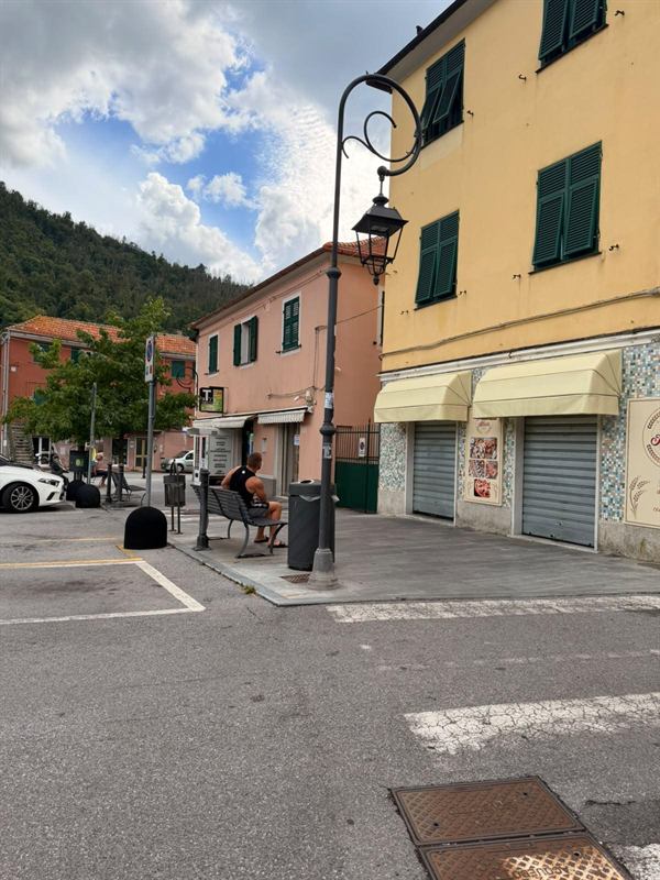 Palazzina gialla con persiane verdi e panificio al piano terra, panchina sotto il lampione